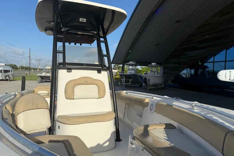 Slide: The Image of 2016 Key West 239 FS boat interior with seating and console, parked near a modern building. - 14