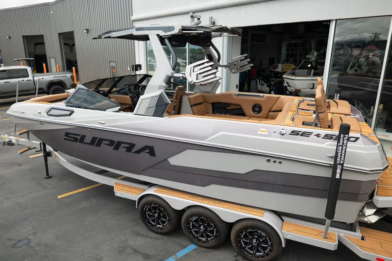 Slide: The Image of 2025 Supra SE 550 boat on trailer, sleek design, gray and tan color scheme, parked outside dealership. - 4