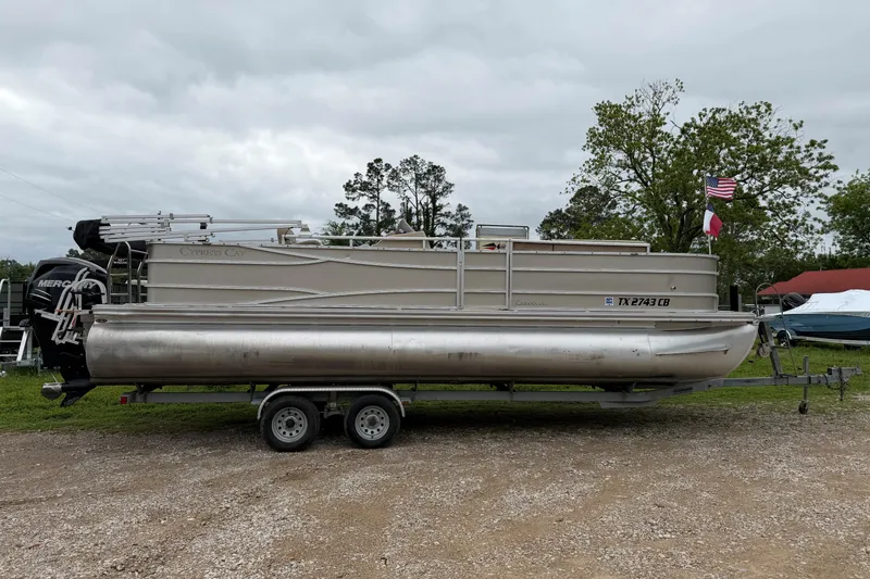 The Image of 2013 Cypress Cay Tritoon Cabana 240 on trailer, parked outdoors with flags. - 0