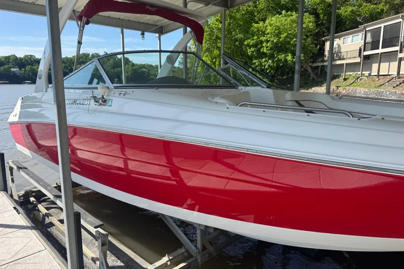 The Image of 2006 Rinker 282 Captiva Bowrider with red and white exterior docked by a lake. - 0