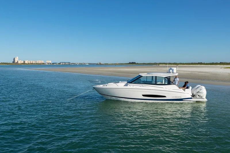 Slide: The Image of 2026 Regal 36 XO boat cruising near a sandy shoreline under a clear blue sky. - 2