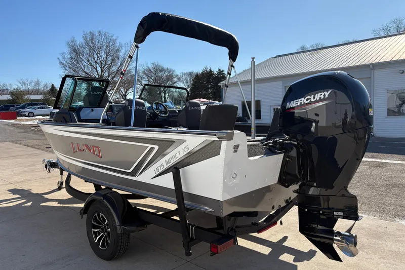 Slide: The Image of 2026 Lund 1875 Impact XS Sport boat with Mercury outboard motor, parked outdoors. - 4
