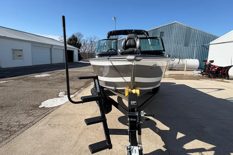 Slide: The Image of 2026 Lund 1875 Impact XS Sport boat on trailer, parked outdoors near industrial buildings. - 7