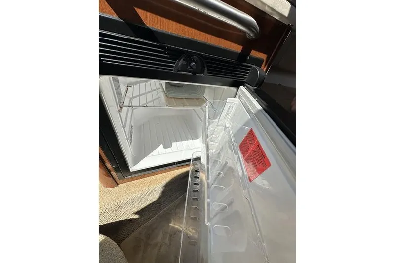 Slide: The Image of Open refrigerator inside 2010 Sea Ray 240 Sundancer boat, showcasing interior storage space. - 28