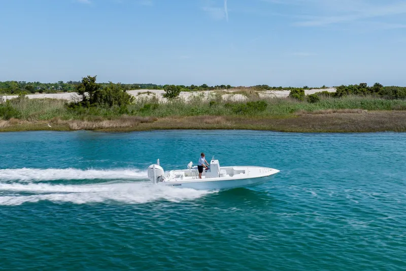 Slide: The Image of 2024 Contender 23 Bay boat cruising on clear blue water near a grassy shoreline. - 44