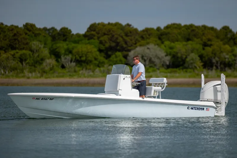 Slide: The Image of 2024 Contender 23 Bay boat cruising on calm water with lush green background. - 6