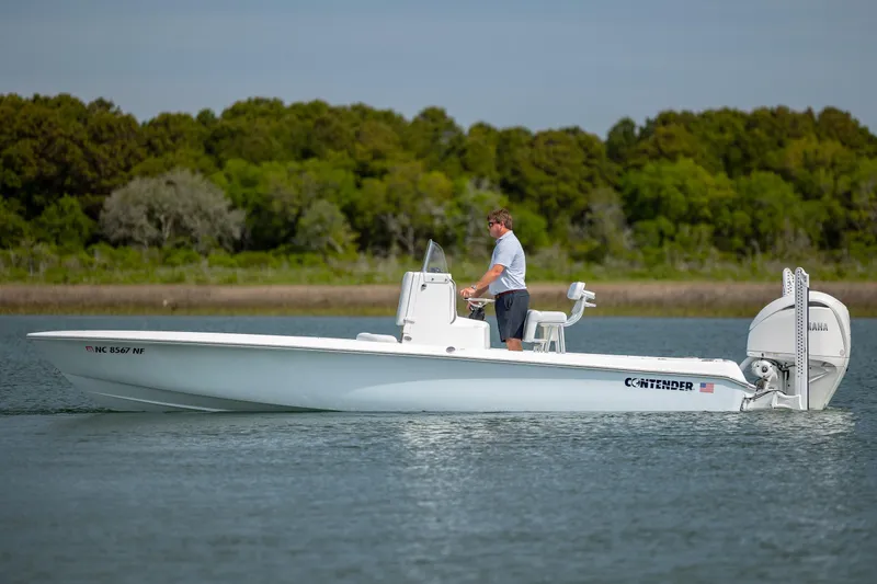 Slide: The Image of 2024 Contender 23 Bay boat on water, man steering, lush green background. - 7