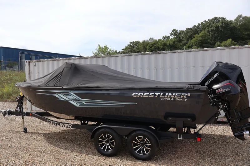 Slide: The Image of 2026 Crestliner 2050 Authority boat with cover, parked on gravel near a container. - 60