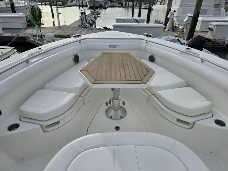 Slide: The Image of 2015 Boston Whaler 350 Outrage boat with cushioned seating and wooden table in marina. - 22