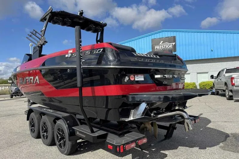 Slide: The Image of 2022 Supra SE boat with red and black design on a trailer, parked outside a blue building. - 8