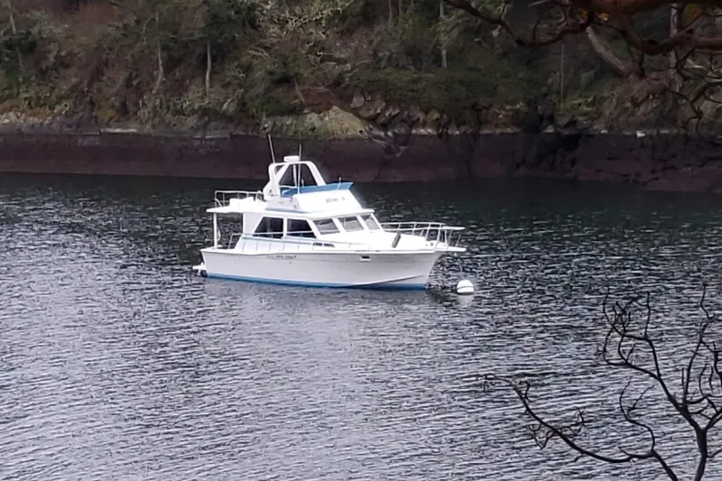 Slide: The Image of 1977 Uniflite 42 Convertible boat anchored in a serene, wooded lake setting. - 23