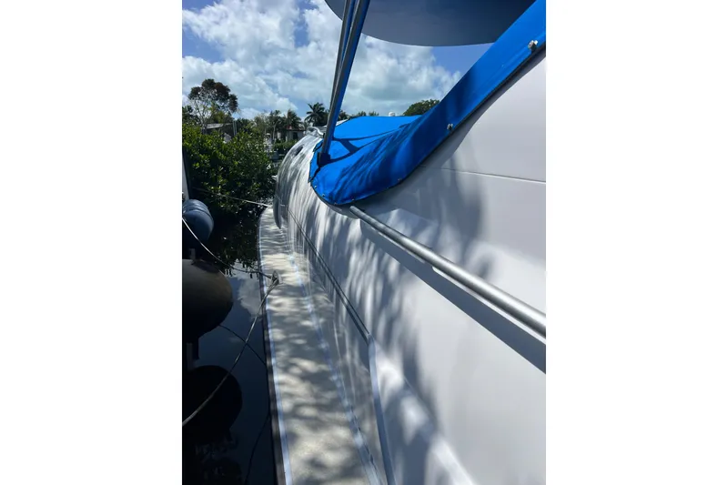 Slide: The Image of 2020 Paritetboat Looker with blue canopy, docked near lush greenery under a cloudy sky. - 15