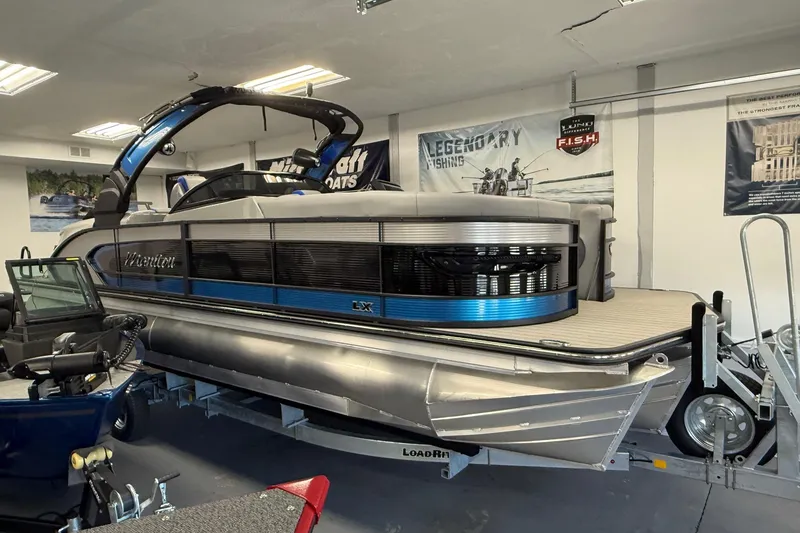 The Image of 2026 Manitou 25 LX RFW pontoon boat displayed indoors on a trailer. - 1