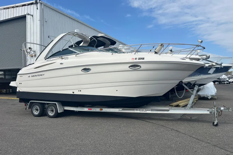 The Image of 2006 Monterey 270 Cruiser boat on trailer, parked outdoors near a warehouse. - 0