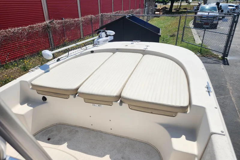 Slide: The Image of 2019 Carolina Skiff 218 DLV boat with cushioned seating, parked near a red fence. - 9