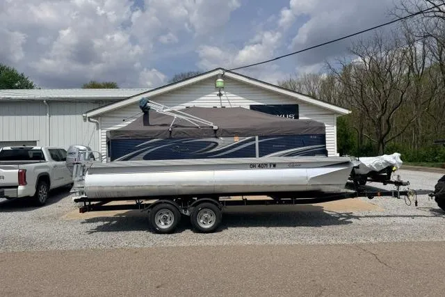 The Image of 2019 Quest Adventure 818 pontoon boat on trailer, parked outside a building under cloudy skies. - 1