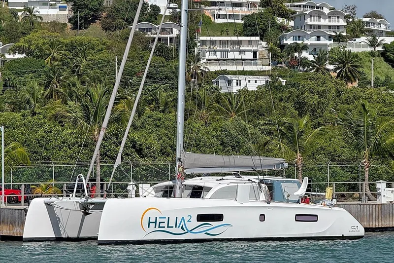 The Image of 2022 Outremer 51 catamaran docked, lush greenery and hillside homes in the background. - 0