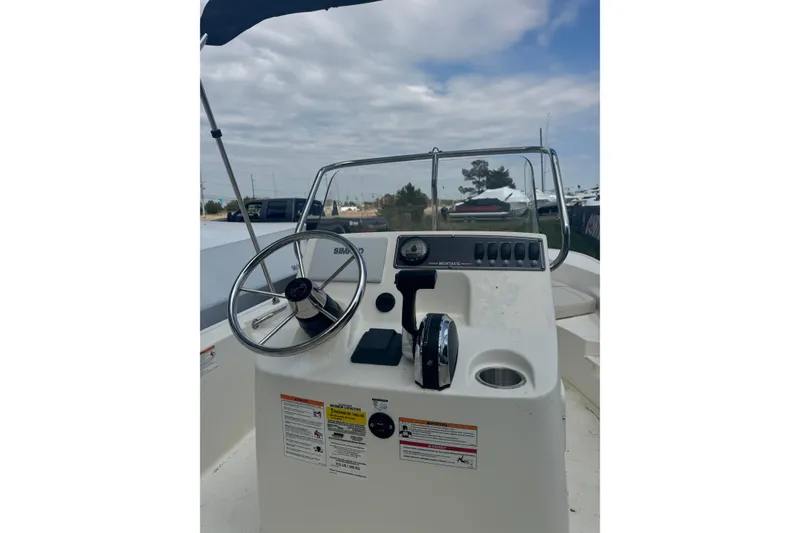 Slide: The Image of 2026 Boston Whaler 170 Montauk boat console with steering wheel and controls under cloudy sky. - 32