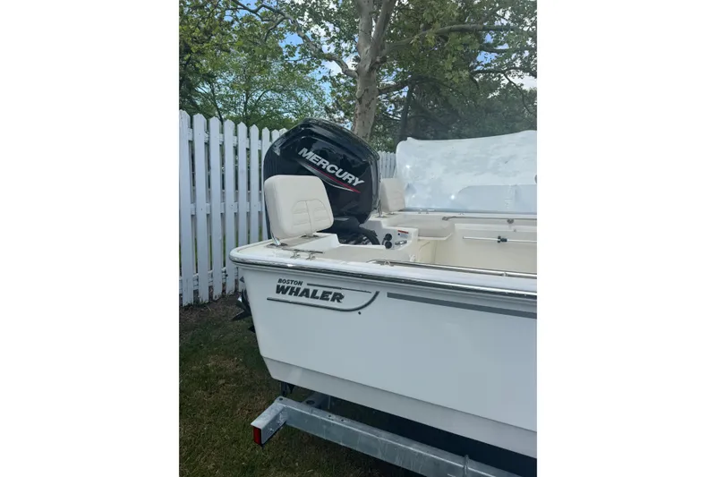 Slide: The Image of 2026 Boston Whaler 170 Montauk boat with Mercury engine, parked near white fence. - 33