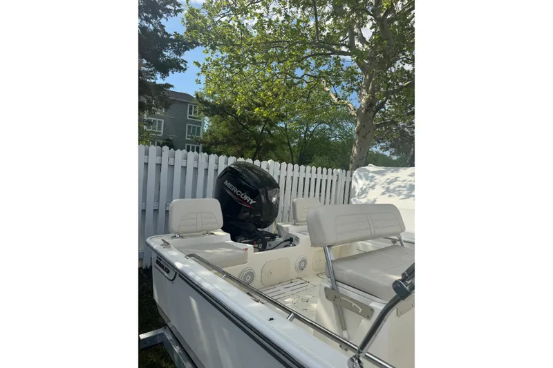 Slide: The Image of 2026 Boston Whaler 170 Montauk boat with Mercury engine, parked near white fence. - 34