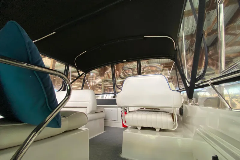 Slide: The Image of Interior of a 1991 Carver 28 Command Bridge boat with white seating and blue cushions. - 36