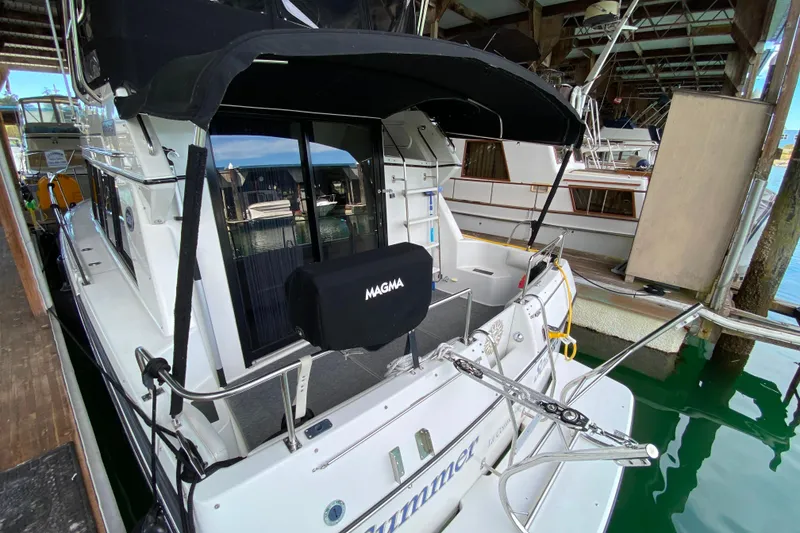 Slide: The Image of 1991 Carver 28 Command Bridge docked, featuring a covered deck and visible marina surroundings. - 60