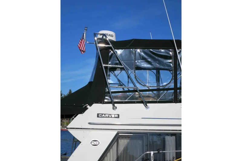 Slide: The Image of 1991 Carver 28 Command Bridge boat with American flag, clear canopy, and blue sky background. - 77