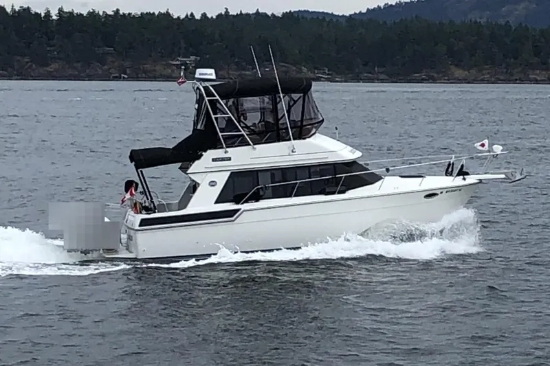Slide: The Image of 1991 Carver 28 Command Bridge cruising on a lake with forested shoreline. - 78