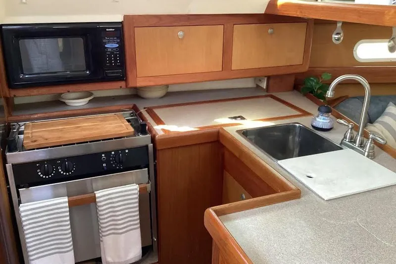 Slide: The Image of 1999 Hunter 340 yacht kitchen with stove, microwave, sink, and wooden cabinetry. - 18