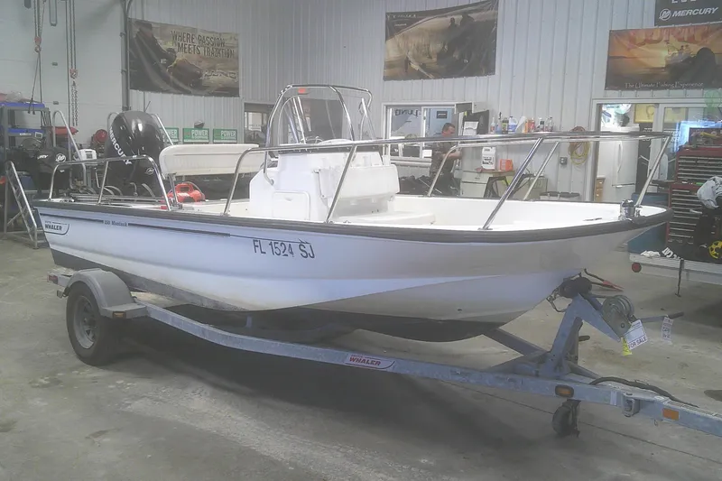 The Image of 2012 Boston Whaler 150 Montauk boat on trailer in a workshop setting. - 1