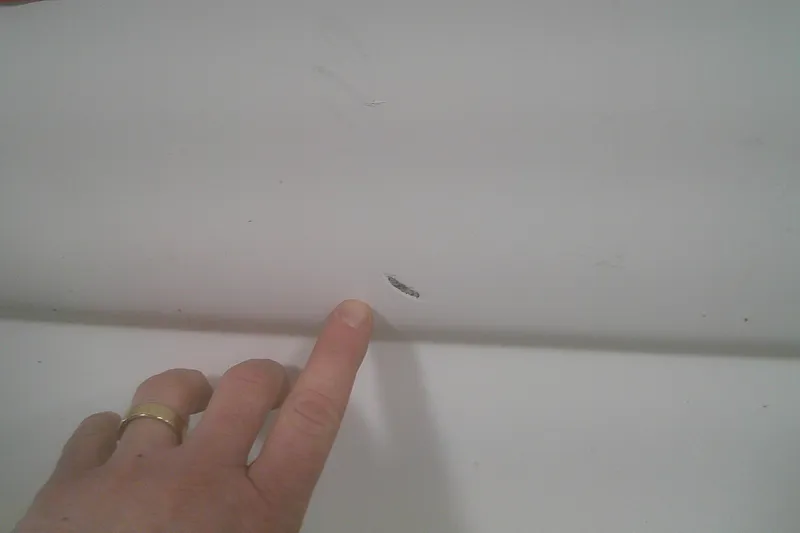 Slide: The Image of A hand pointing at a small scratch on a 2012 Boston Whaler 150 Montauk boat. - 16