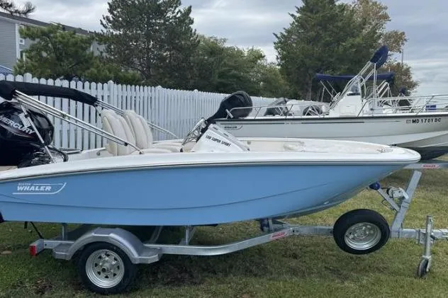 The Image of 2026 Boston Whaler 130 Super Sport boat on trailer, parked on grass near white fence. - 0