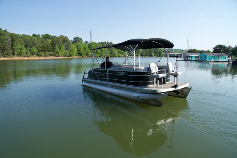 Slide: The Image of 2018 Godfrey Sweetwater20 pontoon boat on a serene lake with lush green surroundings. - 10