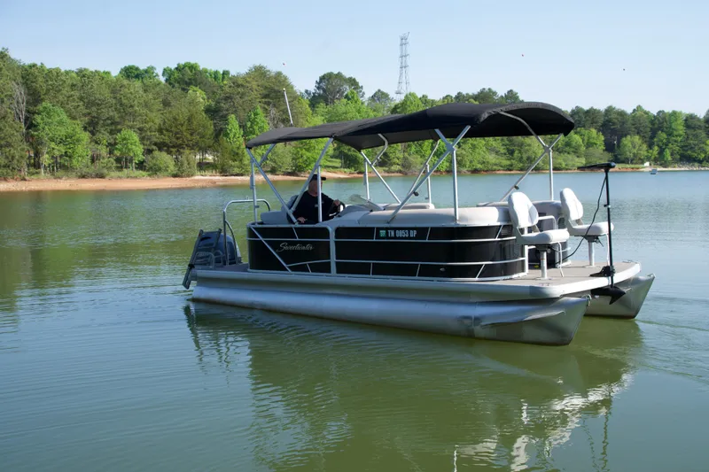 Slide: The Image of 2018 Godfrey Sweetwater20 pontoon boat on a serene lake with lush green surroundings. - 11