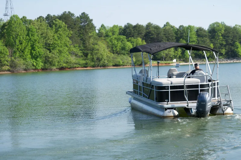 Slide: The Image of 2018 Godfrey Sweetwater20 pontoon boat cruising on a scenic lake with lush green trees. - 14