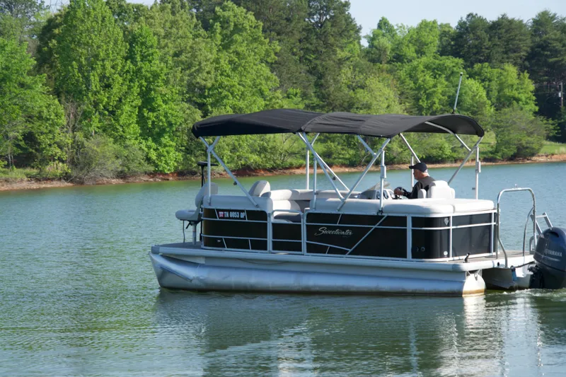 Slide: The Image of 2018 Godfrey Sweetwater20 pontoon boat cruising on a serene lake with lush green trees. - 15