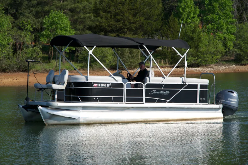 Slide: The Image of 2018 Godfrey Sweetwater20 pontoon boat cruising on a serene lake with lush green surroundings. - 16