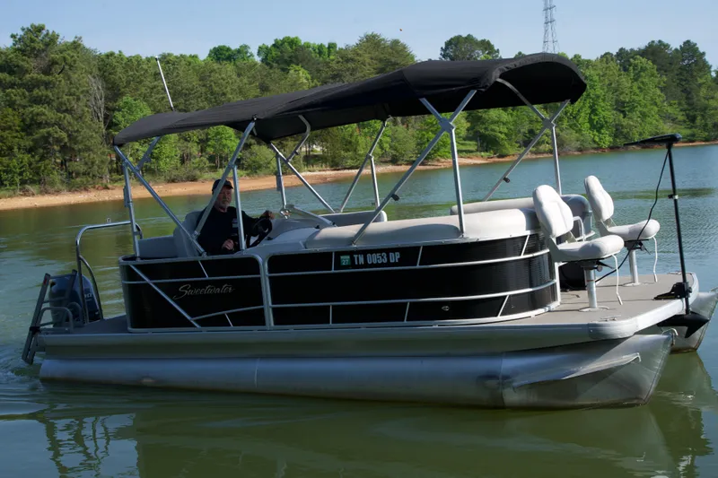 Slide: The Image of 2018 Godfrey Sweetwater20 pontoon boat on a serene lake with lush green surroundings. - 20