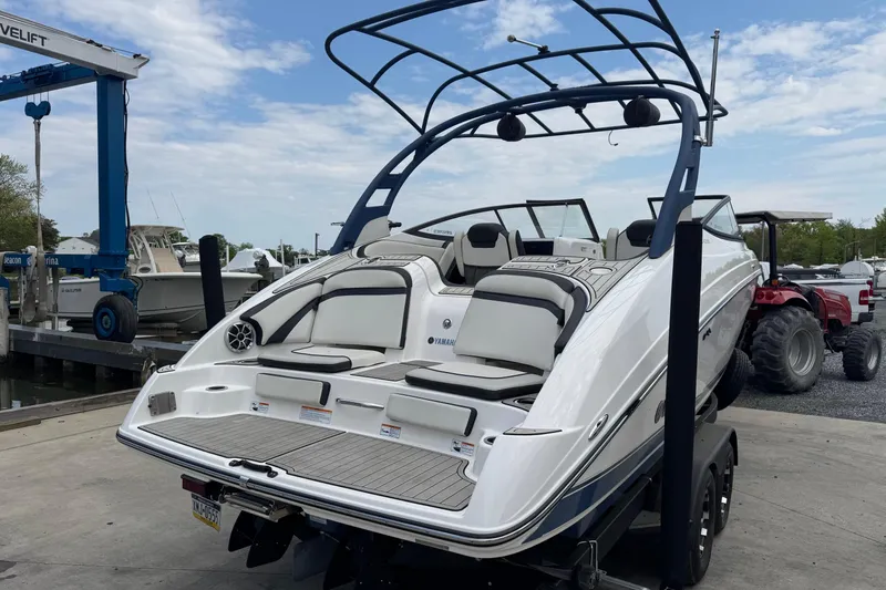Slide: The Image of 2020 Yamaha Boats 242SE on trailer at marina, showcasing sleek design and spacious seating. - 2