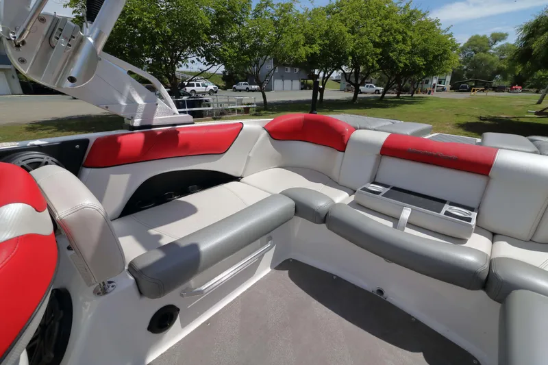 Slide: The Image of 2014 MasterCraft X-25 boat interior with red and gray seating, cup holders, and lush surroundings. - 18
