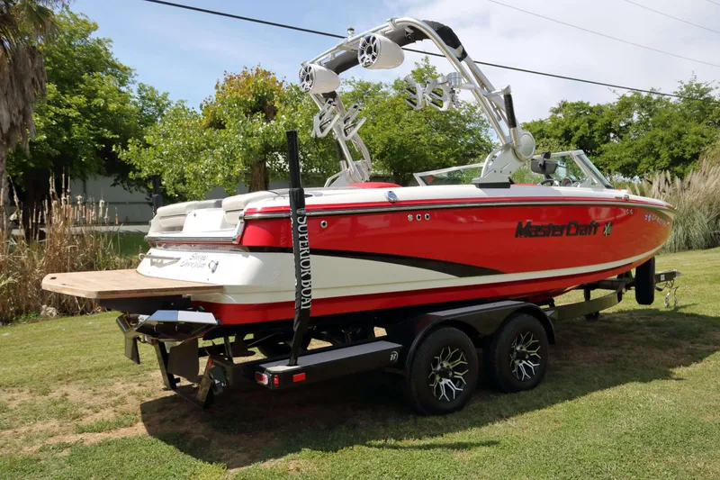 Slide: The Image of 2014 MasterCraft X-25 boat on trailer, red and white design, parked on grass. - 2