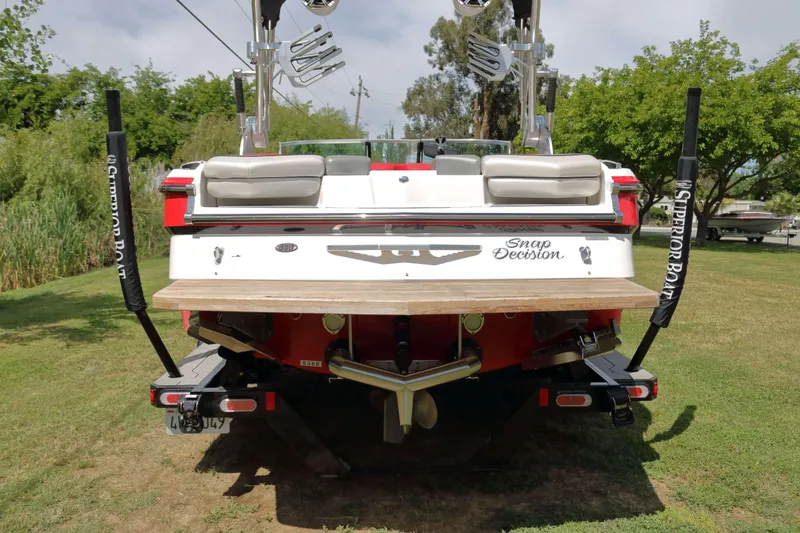 Slide: The Image of 2014 MasterCraft X-25 boat rear view on grass, showcasing wakeboard racks and swim platform. - 3