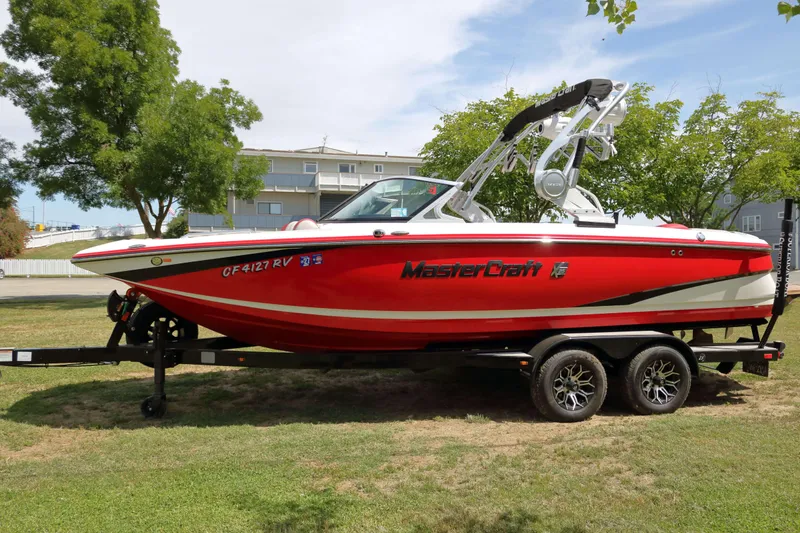 Slide: The Image of 2014 MasterCraft X-25 boat in vibrant red on a trailer, parked on grass. - 6
