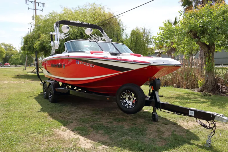 Slide: The Image of 2014 MasterCraft X-25 boat on trailer, parked on grass, with trees in background. - 8
