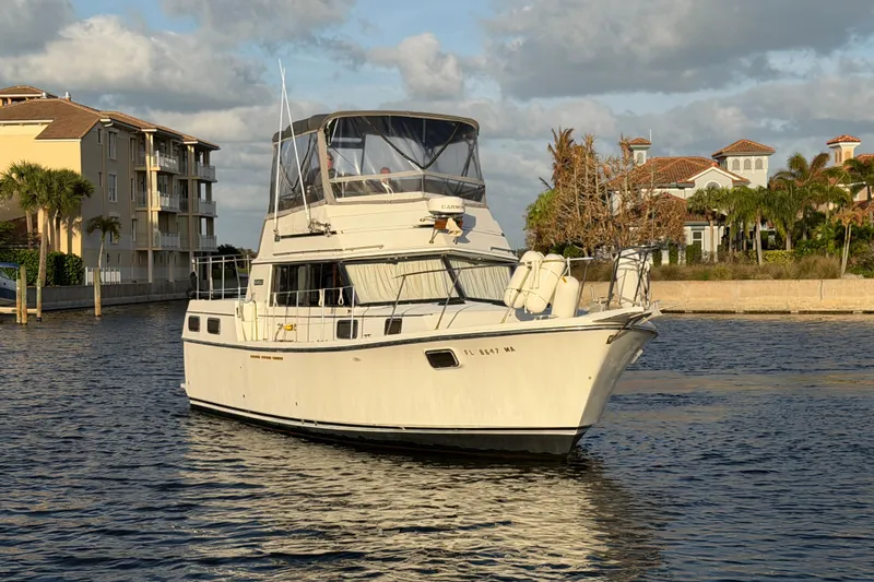 Slide: The Image of 1984 Carver 3607 Aft Cabin Motor Yacht cruising near waterfront homes under a partly cloudy sky. - 3