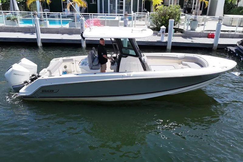 Slide: The Image of 2024 Boston Whaler 280 Outrage boat cruising in a marina with a person at the helm. - 14