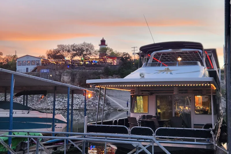 Slide: The Image of Houseboat docked at sunset near a lively waterfront area, featuring a Sharpe 85 model from 2000. - 3