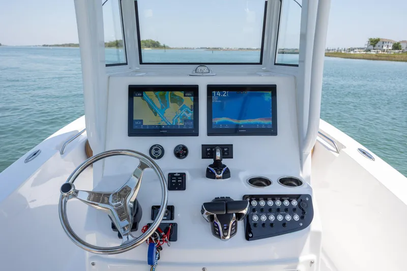 Slide: The Image of 2024 NauticStar 252 Legacy boat dashboard with navigation screens and steering wheel on open water. - 20