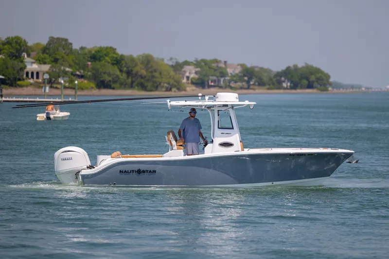 Slide: The Image of 2024 NauticStar 252 Legacy boat cruising on a calm lake with scenic shoreline. - 9