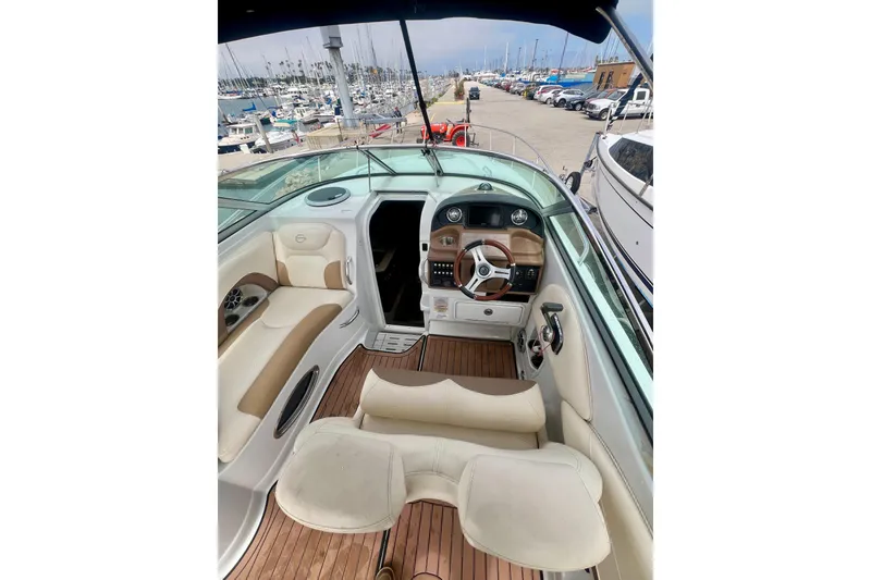 Slide: The Image of 2021 Crownline 264 CR boat interior with beige seating and wooden flooring at a marina. - 6